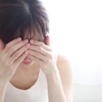 寝室のベッドで頭を押さえる女性