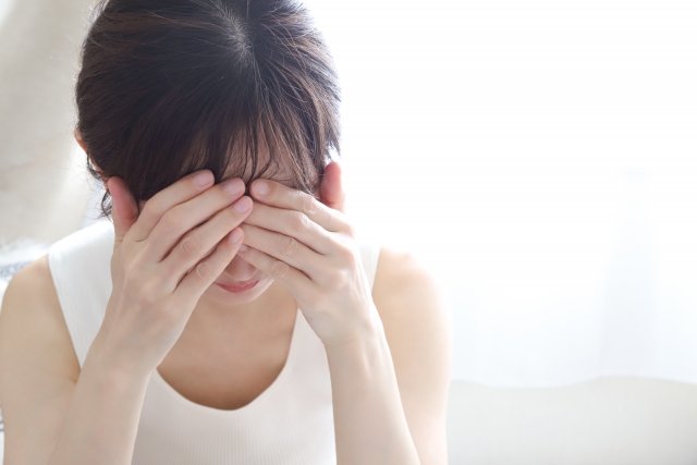寝室のベッドで頭を押さえる女性